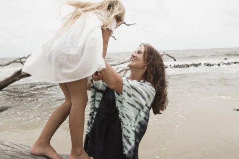 Caucasian mother and daughter playing on driftwood on beach