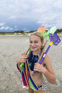 Caucasian girl on beach carrying net and shovels