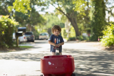 Caucasian boy pulling red wagon in street