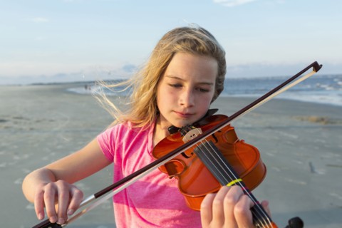 Caucasian girl playing violin on windy beach