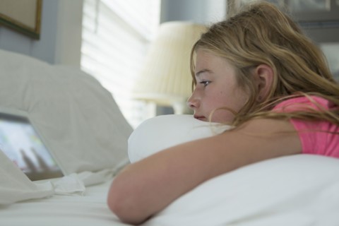Caucasian girl laying on bed watching digital tablet