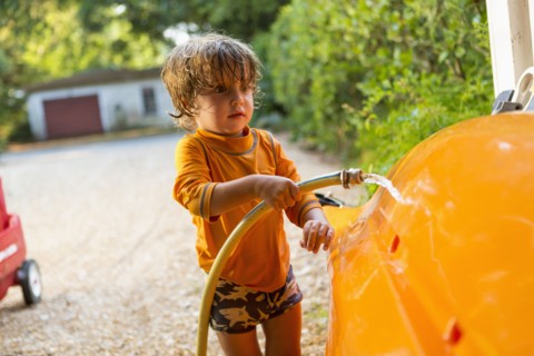 Caucasian boy washing kayak with hose