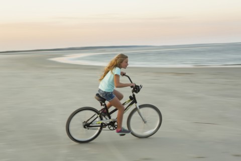 Caucasian girl riding bicycle on beach