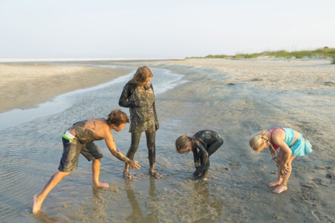 Caucasian brother and sisters covered in mud playing on beach