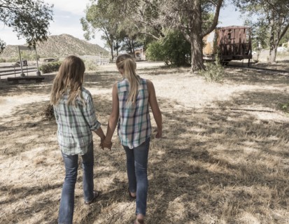 Caucasian girls holding hands walking in field
