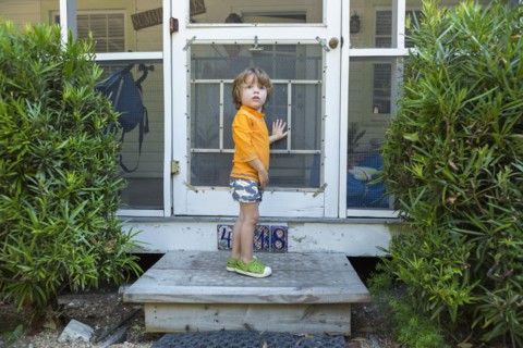 Curious Caucasian boy standing at screen door