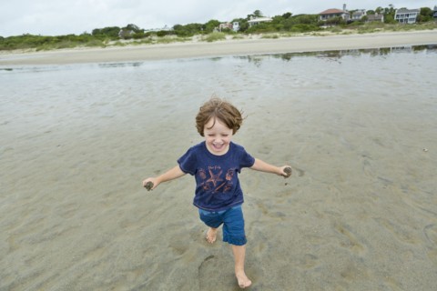 Caucasian boy running on beach carrying sand