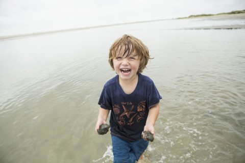 Caucasian boy waiting in ocean carrying sand