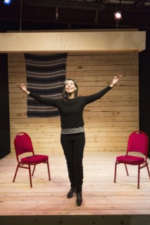 Hispanic woman with arms raised on theater stage
