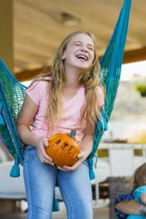 Laughing Caucasian girl in hammock holding pumpkin