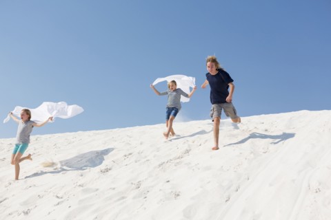 Caucasian boy and girls running on sand dune