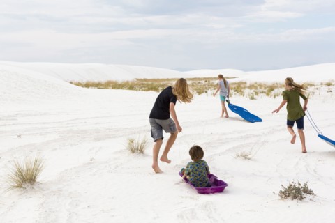 Caucasian boys and girls playing on sleds in sand