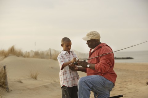 African father and son on beach with fishing gear