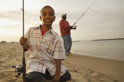 African father and son on beach with fishing gear
