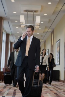 Businessman talking on cell phone and pulling suitcase down corridor