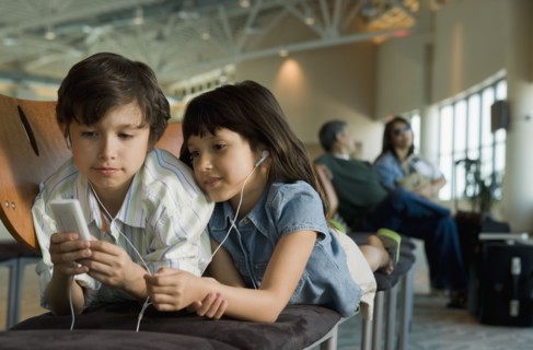 Hispanic brother and sister listening to mp3 player in airport
