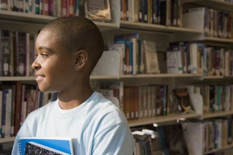 Mixed race boy holding books in library