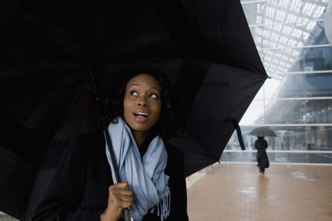 African businesswoman holding umbrella in rain