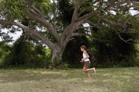Hispanic girl running barefoot through grass