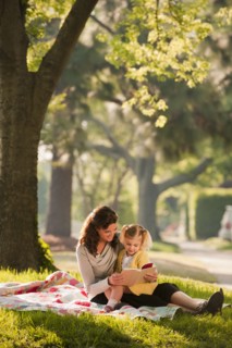 Caucasian mother reading story to daughter in park