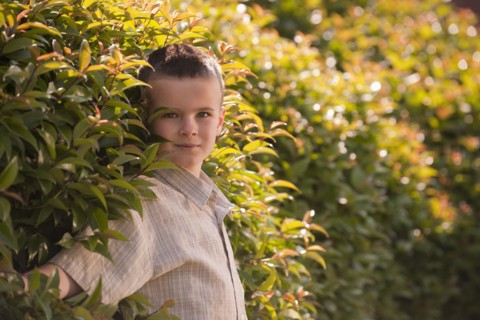 Caucasian boy standing near shrub