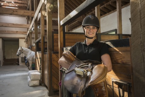 Caucasian girl carrying saddle in horse stable