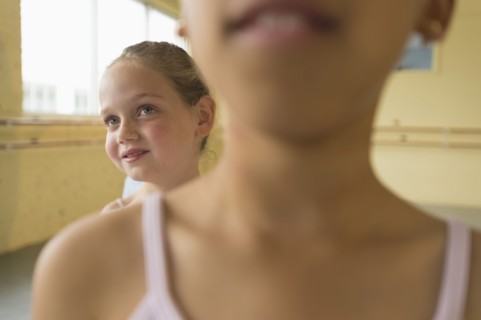 Girl peeking over shoulder of girl in ballet studio