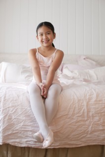 Asian girl in ballet costume sitting on bed