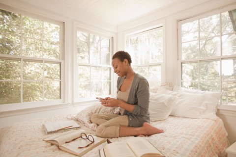 African American woman studying in bed and using cell phone