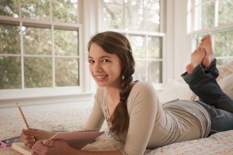 Mixed race girl laying in bed writing in journal