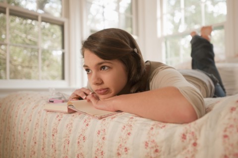 Mixed race girl laying in bed writing in journal