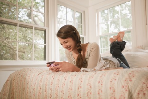 Mixed race girl laying in bed text messaging on cell phone