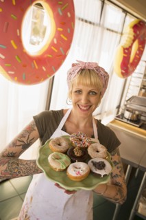 Asian baker holding plate of donuts in bakery
