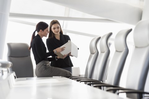 Caucasian businesswomen at conference table reading notepad