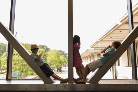 Caucasian boys and girl leaning on beams in airport