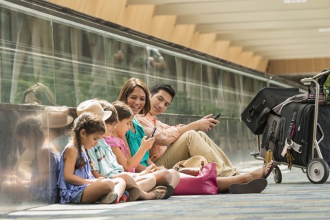 Family waiting on floor of airport using cell phones