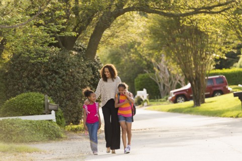 Mother walking in street with daughters wearing backpacks