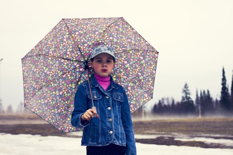 Caucasian girl walking under umbrella in snowy field