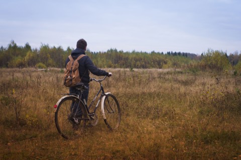 Caucasian man pushing bicycle in field