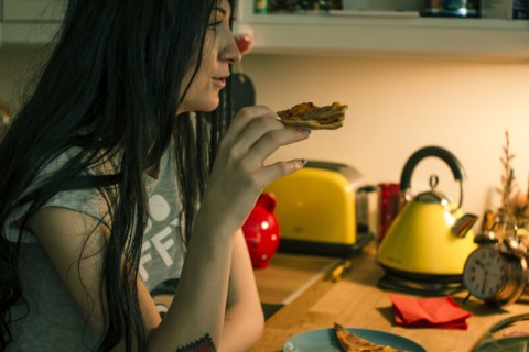 Caucasian woman eating pizza in kitchen