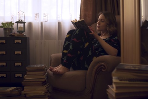 Caucasian woman sitting in armchair reading pile of books