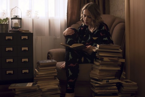 Caucasian woman sitting in armchair reading pile of books