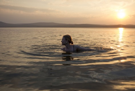 Caucasian woman swimming in lake at sunset