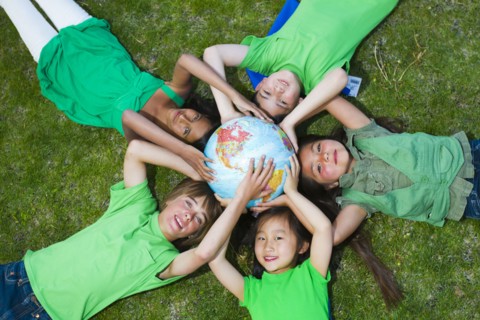 Children laying in grass around globe