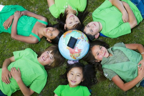 Children laying in grass around globe with solar panel