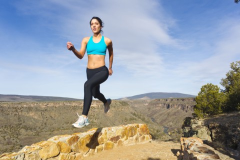 Hispanic woman jumping in mid-air in remote area