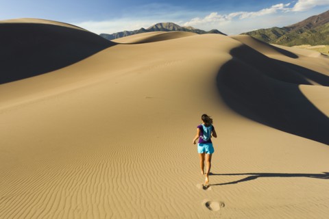 Hispanic woman running on sand dune