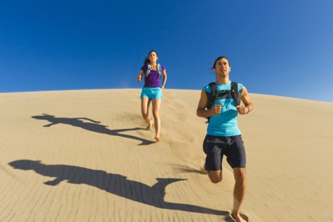 Hispanic couple running on sand dune