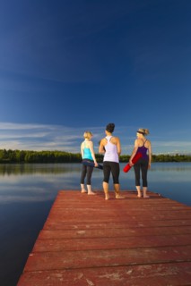 Women holding yoga mats on lake pier