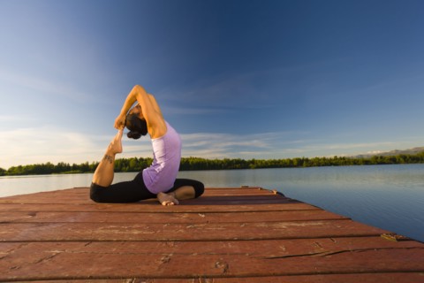Korean woman practicing yoga on lake pier